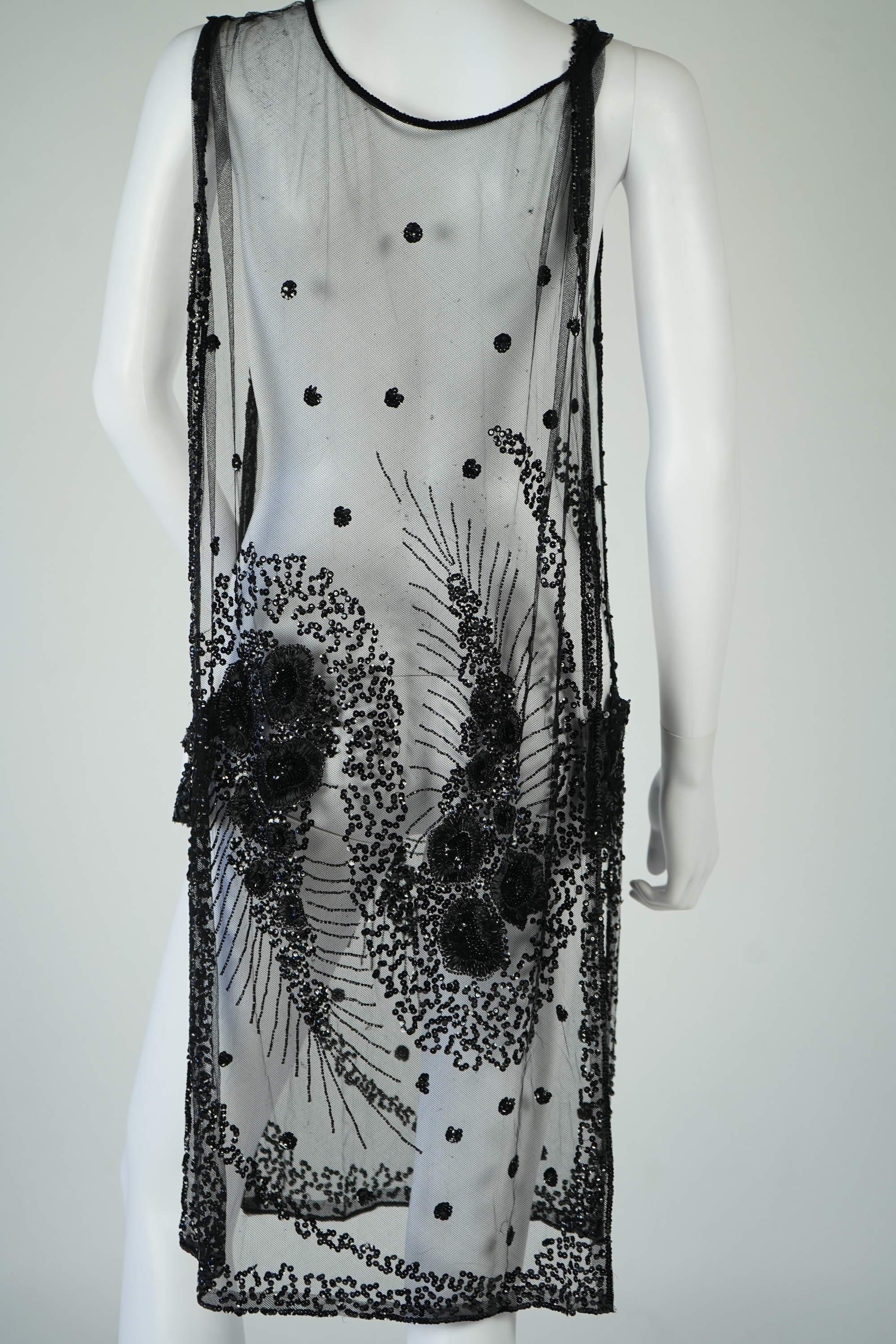 A 1920's black sequin on net tabard, with floral decoration and two side sequinned straps. Length 97cm. Condition - a few sequins have detached but are in a bag for re-attaching.